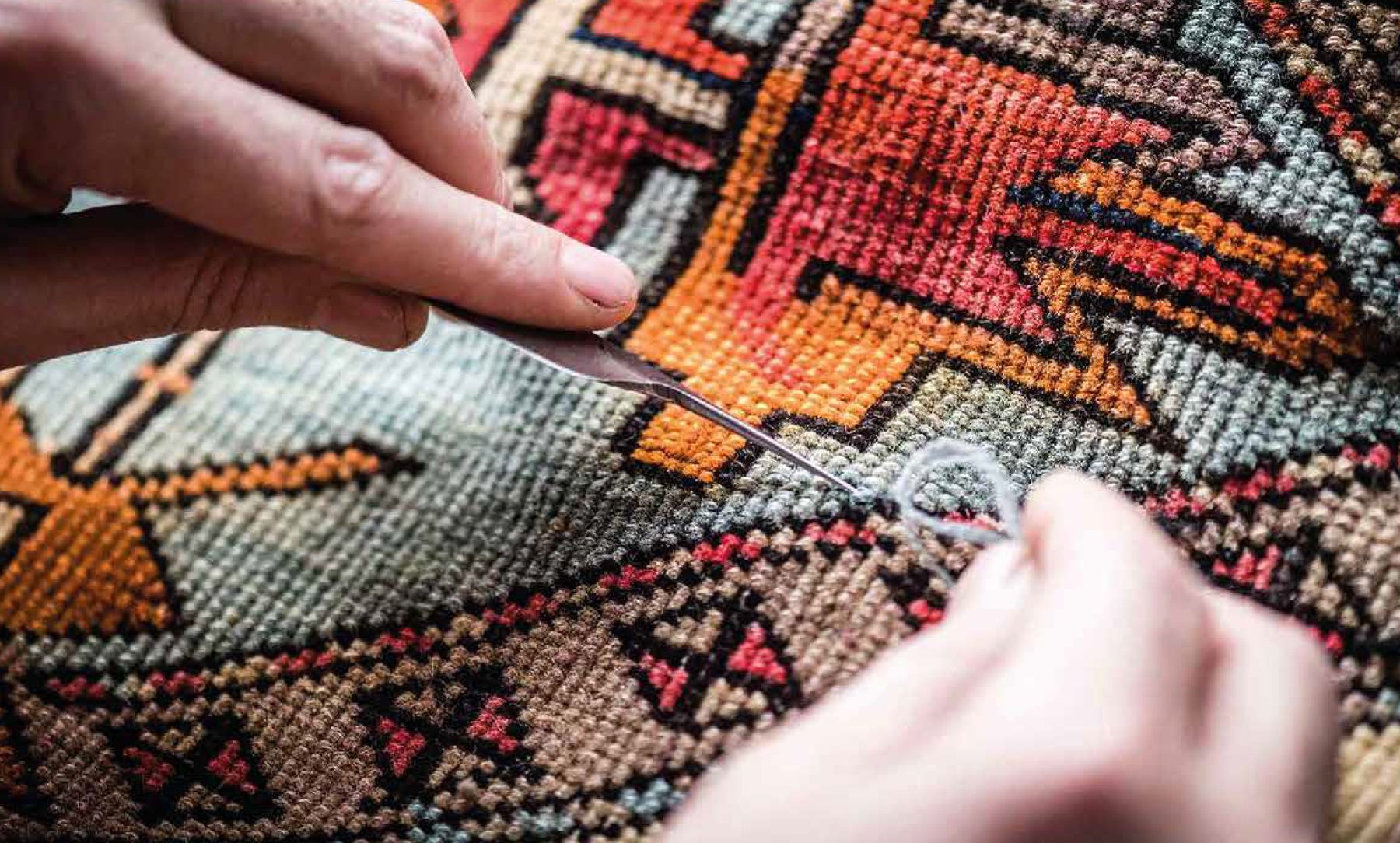 Mains réparant à l’aiguille un kilim aux motifs géométriques